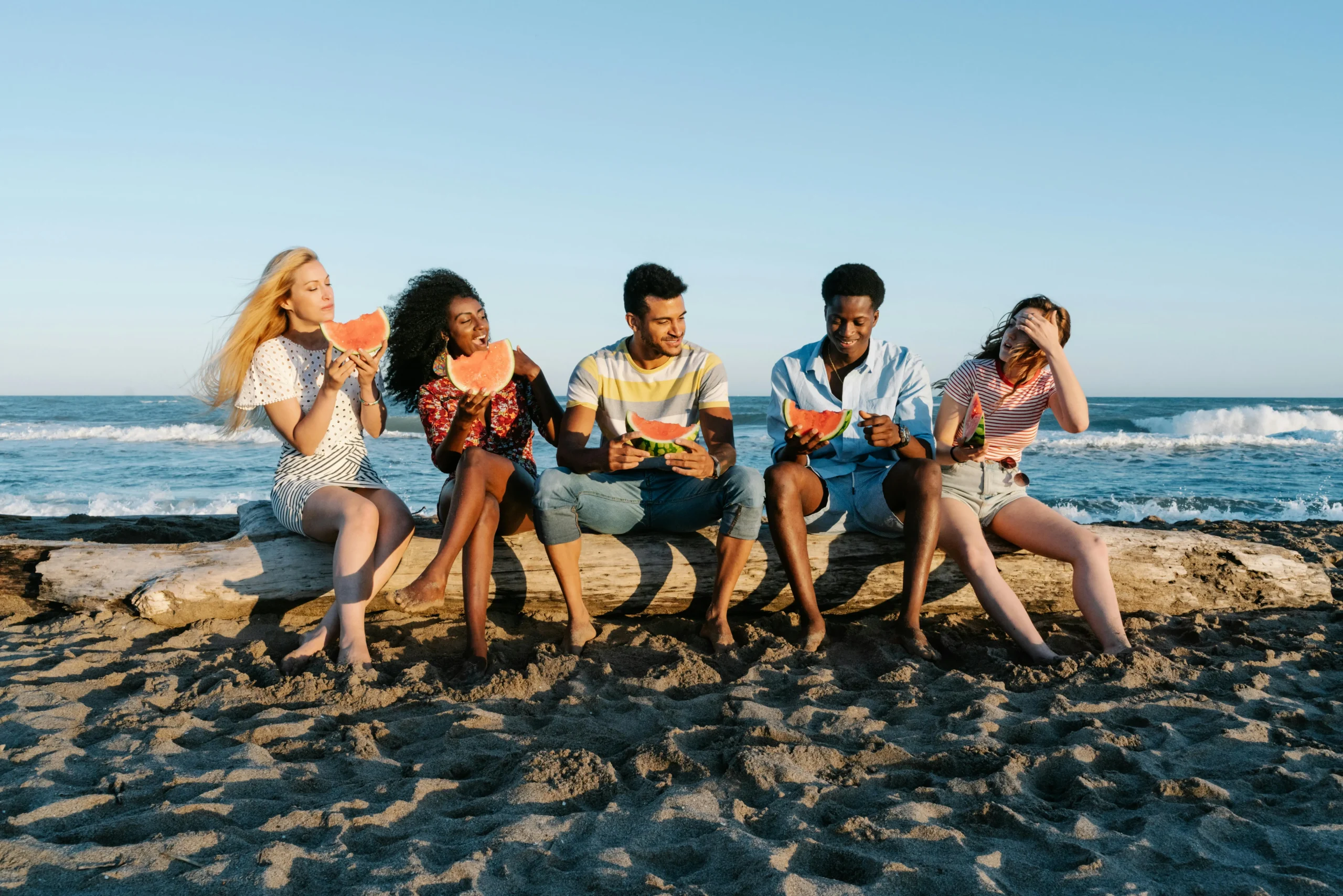 Friends eating watermelon on a log at the beach
