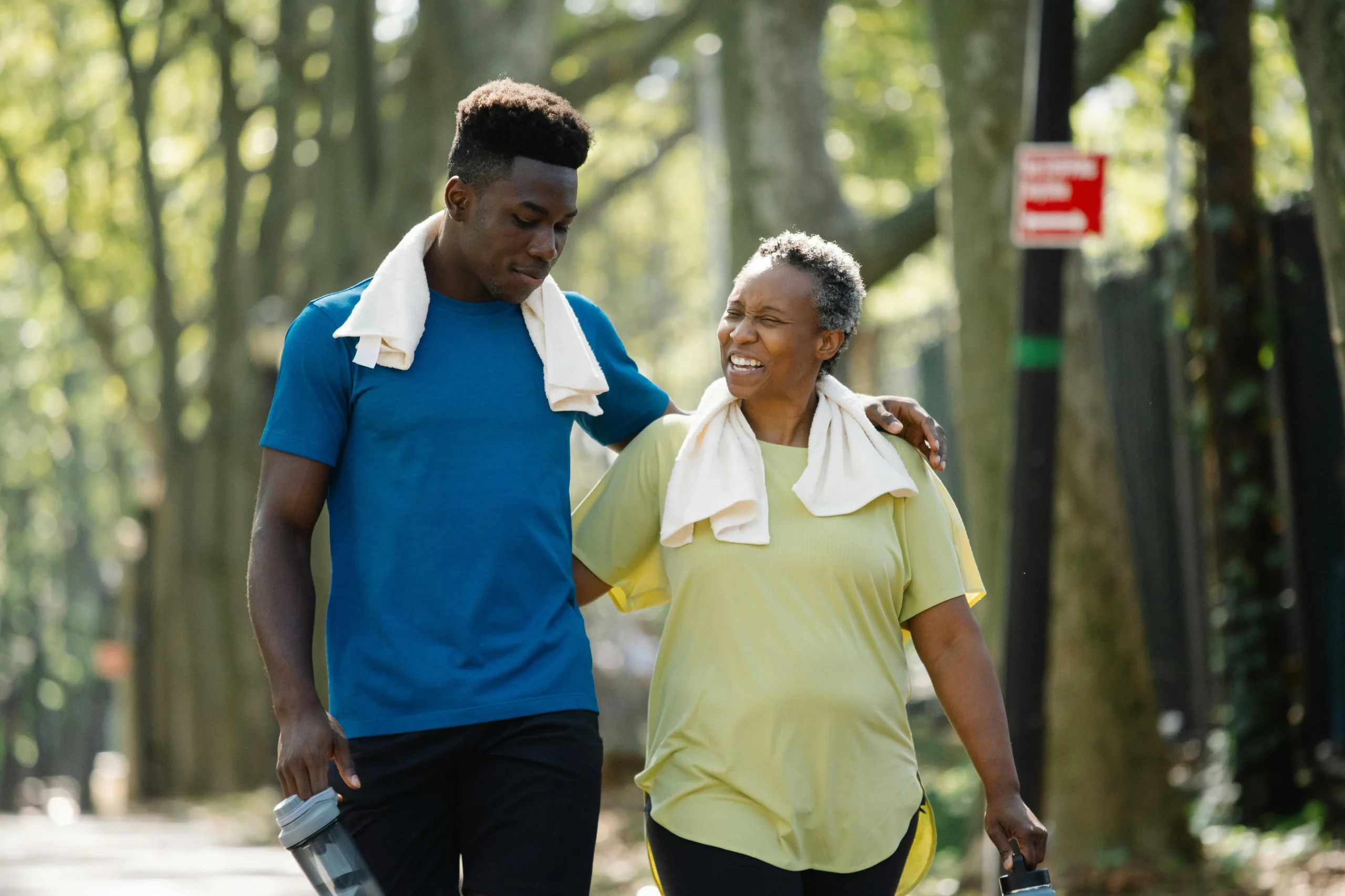 Son in blue shirt with towel around neck walking with mother in green shirt and towel around neck after working out